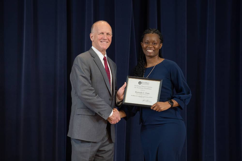Graduate student and Dean Potteiger smiling and posing for a photo with an award